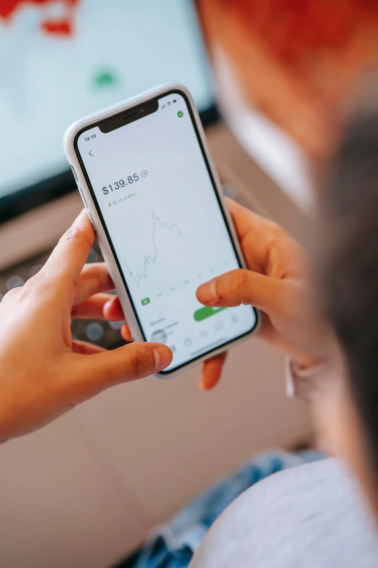 Mão segurando celular com gráfico de ações